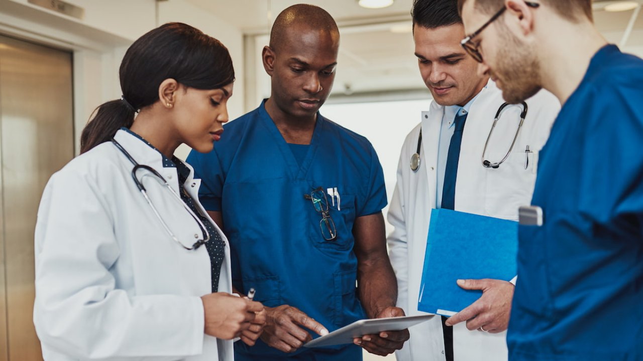 A diverse team of healthcare professionals in discussion over a tablet, reviewing radiopharmaceutical trial data for NETs.